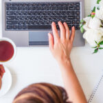 Workspace,With,Girl’s,Hand,On,Laptop,Keyboard,And,Cup,Of